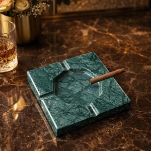 Peut inclure: Cendrier carré en marbre vert avec un cigare. Le cendrier a une surface texturée et un design géométrique. Le cendrier est sur une surface en marbre brun. Un verre de liquide ambré est en arrière-plan.