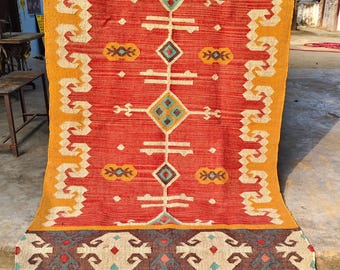 May include: A rectangular, handwoven rug with a vibrant design. The rug features a red central field with geometric patterns in white, teal, and brown. The borders are yellow and brown, with fringed edges. A decorative floor covering.