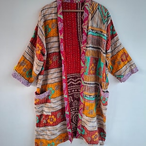 Può includere: Una vestaglia a maniche lunghe con apertura frontale caratterizzata da un design patchwork con strisce orizzontali, motivi floreali e disegni geometrici nei toni del rosso, arancione, giallo, verde acqua e viola. Il capo presenta due tasche frontali.