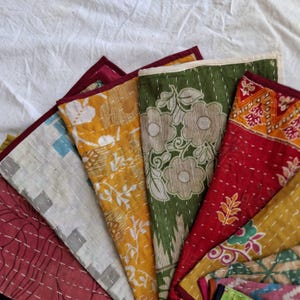 May include: A selection of colourful, handmade fabric items, possibly coasters or small decorative pieces. The items feature various patterns, including floral and geometric designs, with visible stitching and contrasting border colours. The colour palette includes red, yellow, green, and white.