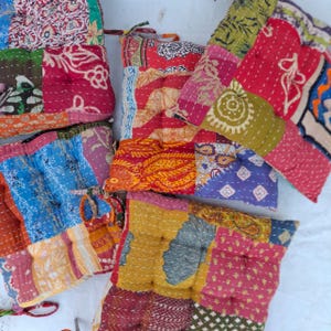 Könnte beinhalten: Eine Sammlung quadratischer Bodenkissen mit Patchwork-Designs aus verschiedenen bunten Stoffen. Jedes Kissen zeigt komplizierte Muster in Rot-, Blau-, Gelb-, Grün- und Orangetönen mit sichtbarer, von Hand genähter Kantha-Steppung.