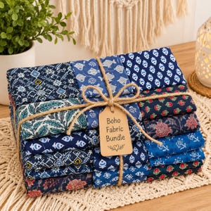 Könnte beinhalten: Ein Stapel gefalteter Stoffquadrate mit verschiedenen blauen, weißen und roten Blumen- und geometrischen Mustern. Das Bündel ist mit braunem Garn verschnürt und enthält ein beiges Papieretikett mit dem Text Boho Fabric Bundle und einem Herz.