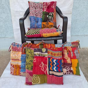 Könnte beinhalten: Eine Sammlung quadratischer Bodenkissen mit einem Patchwork-Design aus verschiedenen bunten Stoffen mit komplizierten Mustern. Jedes Kissen ist mit sichtbaren Nähten gesteppt und verfügt über Stoffbänder an den Ecken zur Befestigung.