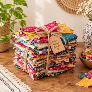 May include: A stack of assorted fabric scraps tied with jute twine, featuring a variety of floral and geometric patterns in vibrant colors like magenta, yellow, blue, and orange. A brown paper tag labeled Fabric Scraps Bundle is attached.