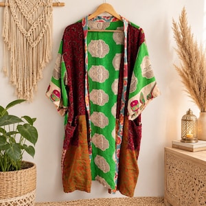 Könnte beinhalten: Ein langärmeliger Kimono-Bademantel mit Patchwork-Design und einem leuchtend grünen Mittelteil, der mit sich wiederholenden Buddha-Kopf-Motiven bedruckt ist. Das Kleidungsstück hat dunkelrote, orangefarbene und gemusterte Bereiche, eine offene Vorderseite und zwei Taschen.