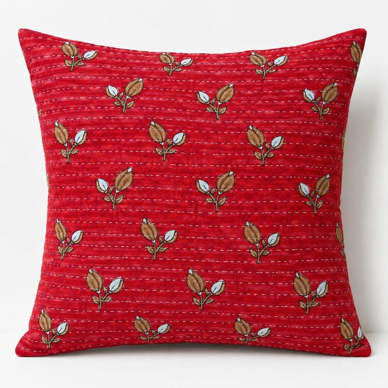 May include: A square throw pillow in a vibrant red fabric featuring a repeating pattern of small brown and white floral buds. The surface is detailed with horizontal rows of white running stitch embroidery that create a quilted texture.