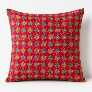 May include: A square throw pillow featuring a vibrant red base color with a repeating pattern of small yellow and teal floral motifs. The fabric has a visible quilted texture with fine white running stitches arranged in a grid across the surface.