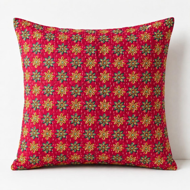 May include: A square throw pillow featuring a vibrant red base color with a repeating pattern of small yellow and teal floral motifs. The fabric has a visible quilted texture with fine white running stitches arranged in a grid across the surface.