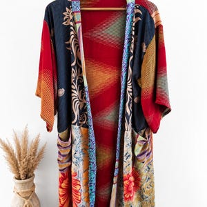 May include: A long-sleeved open-front kimono robe featuring a patchwork design with various patterns including floral motifs, geometric shapes, and stripes in shades of red, navy blue, yellow, and teal, with two front pockets and a solid red interior.