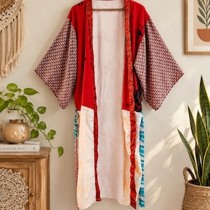 Könnte beinhalten: Ein langer Kimono mit offener Vorderseite im Patchwork-Design mit leuchtend roten Bahnen, schwarz-weiß gemusterten Ärmeln und einem weißen Innenfutter mit dezenten Blattumrissen. Das Kleidungsstück hat weite, dreiviertellange Ärmel.