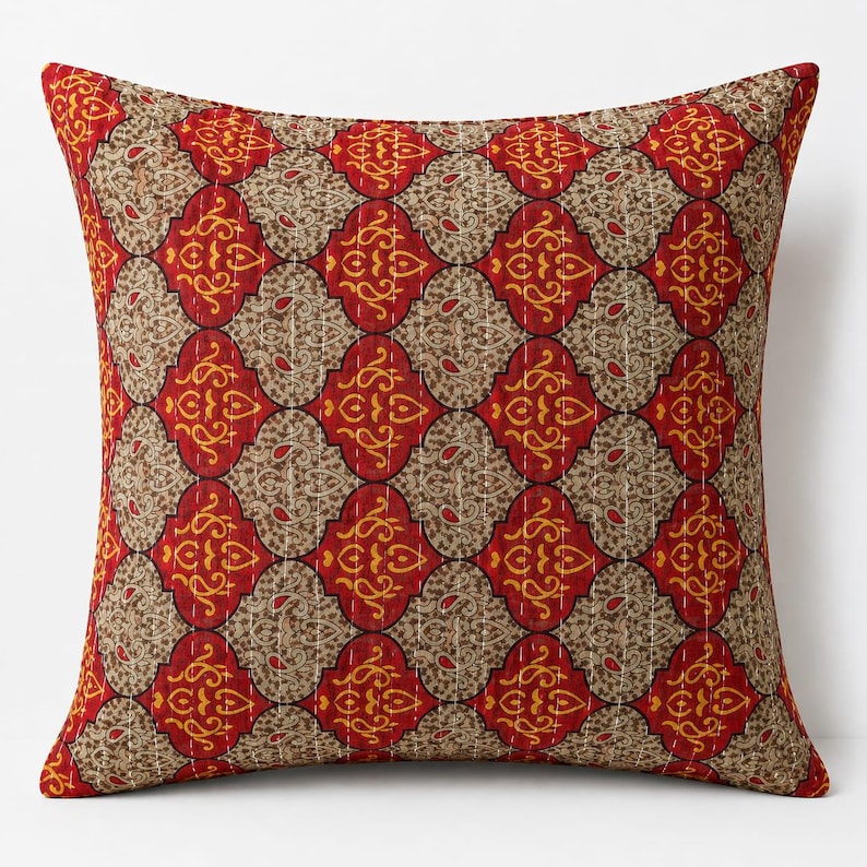 May include: A square throw pillow featuring a repeating pattern of red and beige quatrefoil shapes. The red sections contain yellow swirling paisley motifs, while the beige sections feature intricate brown floral patterns with visible white stitching.