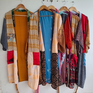 May include: A collection of five open-front kimonos hanging on wooden hangers. Each garment features a unique patchwork design with varied patterns and colours, including mustard yellow, bright blue, deep red, and intricate floral or geometric prints.
