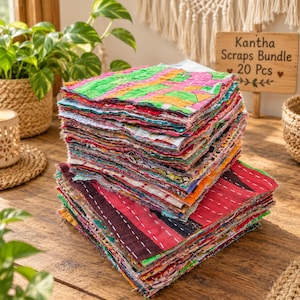 May include: A stack of twenty square fabric scraps featuring various colorful patterns and textures with visible running stitch details. A wooden sign nearby displays the text Kantha Scraps Bundle 20 Pcs with heart icons.