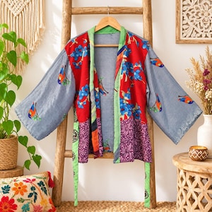 May include: A patchwork kimono jacket featuring a red panel with blue floral patterns, grey sleeves with bird motifs, and purple sections with white botanical prints. The garment has a light green trim and a matching tie belt at the waist.
