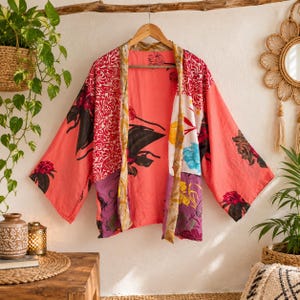 Könnte beinhalten: Ein korallenfarbener Kimono mit offener Vorderseite und Patchwork-Design, das verschiedene florale Muster in Rot-, Gelb-, Blau- und Violetttönen aufweist. Das Kleidungsstück hat weite Ärmel und einen gemusterten Saum an der Vorderseite.