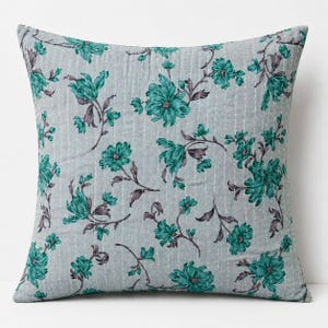 May include: A square throw pillow featuring a light gray fabric base with a repeating pattern of teal flowers and dark gray stems. The surface is accented with vertical white stitched lines that run across the entire front of the pillow.