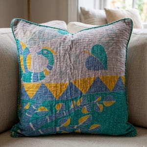 May include: A square throw pillow featuring a quilted texture with visible white stitching. The design displays a stylized peacock in blue, yellow, and teal, alongside a large leaf, a yellow triangular border, and a lower section with leafy branches.
