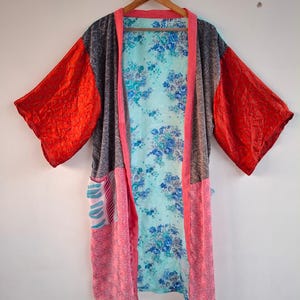 May include: A patchwork kimono robe featuring a light blue interior with a blue floral pattern. The exterior panels consist of dark gray fabric, bright red sleeves, and pink patterned lower sections with a pink trim along the front opening.