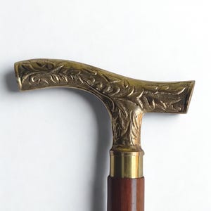 Puede incluir: Bastón de paseo vintage con empuñadura de latón y caña de madera marrón oscuro. La empuñadura de latón es curva y presenta un diseño floral ornamentado. La empuñadura del bastón mide 15 cm de ancho. Un accesorio clásico.