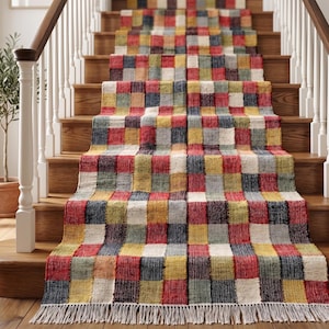 Könnte beinhalten: Ein farbenfroher Treppenläufer mit Patchwork-Design. Der Läufer zeigt ein sich wiederholendes Muster aus roten, gelben, blauen, grünen und cremefarbenen Quadraten. Der Läufer hat einen Fransen am unteren Ende und ist auf Holztreppen installiert.