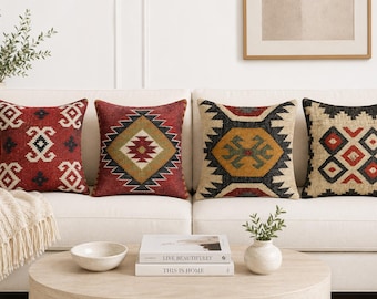 May include: Four square throw pillows featuring intricate geometric patterns in shades of red, black, tan, and mustard yellow. Each pillow displays a unique woven design with symmetrical shapes, lines, and diamonds, arranged side by side on a sofa.