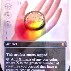 May include: A White Lotus Tile card from the Magic: The Gathering trading card game. The card features a circular design with a white lotus flower. The card text reads "Artifact" and includes game instructions. The card is held in a hand.