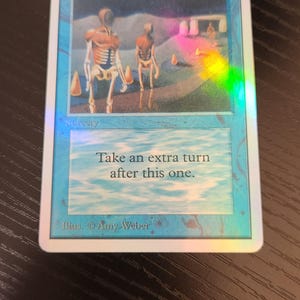 Pu&ograve; includere: Una carta olografica di Magic: The Gathering intitolata "Time Walk". La carta presenta un'illustrazione di due figure scheletriche in un paesaggio surreale. Il testo sulla carta recita "Fai un turno extra dopo questo."