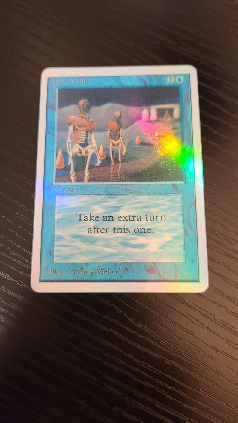 Pu&ograve; includere: Una carta olografica di Magic: The Gathering intitolata "Time Walk". La carta presenta un'illustrazione di due figure scheletriche in un paesaggio surreale. Il testo sulla carta recita "Fai un turno extra dopo questo."