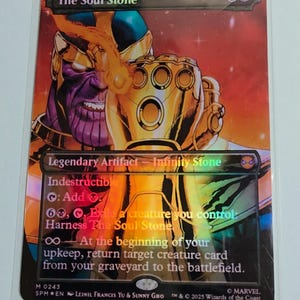 May include: A collectible card featuring Thanos with the Infinity Gauntlet. The card is titled "The Soul Stone" and includes game text. The artwork is vibrant with purple, gold, and red hues, and the card is encased in a protective sleeve.