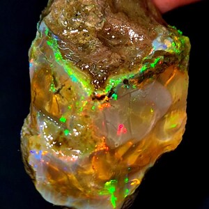 May include: Rough opal gemstone with a brown matrix and vibrant flashes of green, orange, and red. The raw stone displays a play of color, showcasing its natural beauty. A unique specimen for collectors or jewelry making.