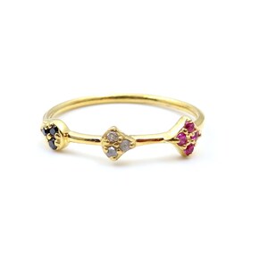 Op de afbeelding: Een delicate gouden ring met drie decoratieve clusters. Eén cluster heeft zwarte stenen, het midden heeft heldere stenen en de derde heeft roze stenen. De ring is geplaatst tegen een witte achtergrond.