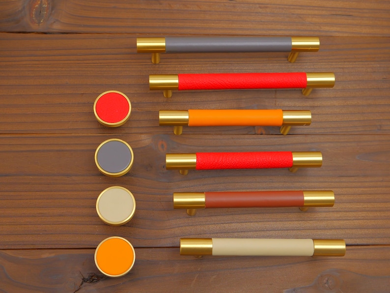 Puede incluir: Un conjunto de herrajes para armarios, que incluye tiradores y pomos redondos. Los tiradores tienen extremos dorados y centros envueltos en cuero de colores (gris, rojo, naranja y marr&oacute;n). Los pomos tienen colores a juego.