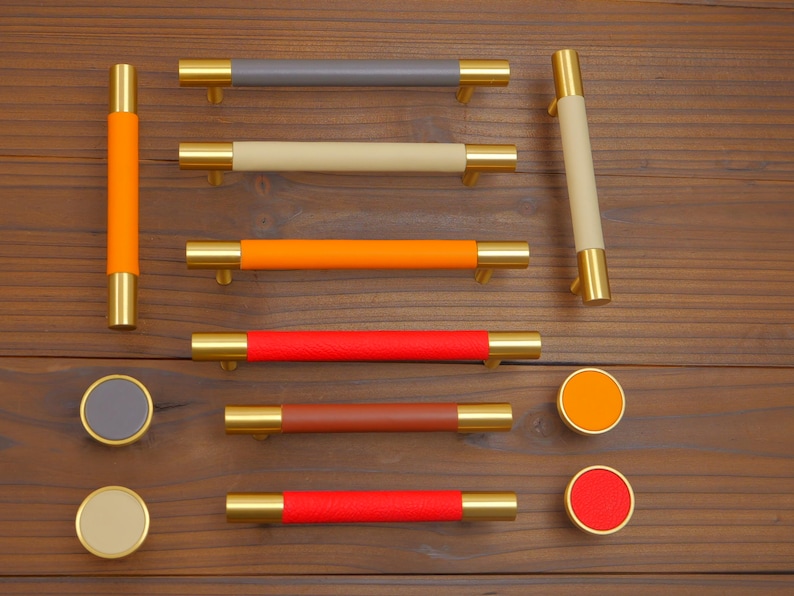 Puede incluir: Una colecci&oacute;n de herrajes para armarios, que incluye tiradores y pomos para cajones. Los tiradores presentan extremos met&aacute;licos dorados y secciones centrales envueltas en cuero de colores en tonos grises, beige, naranja, rojo y marr&oacute;n. Tambi&eacute;n se incluyen pomos redondos.