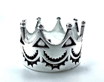 Könnte beinhalten: Silberfarbener Kronenring mit detailliertem Design. Der Ring hat abwechselnd dreieckige und sonnenartige Muster um das Band und ist mit abgerundeten Spitzen versehen.