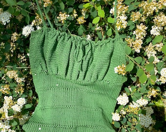 May include: A green knitted tank top with a square neckline and thin straps. The top has a gathered detail at the bust and a fitted bodice.
