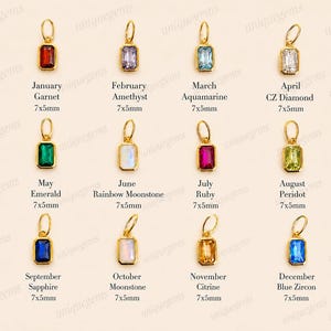 May include: A collection of twelve rectangular gold-framed pendants, each featuring a different colored gemstone representing a birth month. The stones are labeled with their month, name, and 7x5mm dimensions, including garnet, amethyst, aquamarine, diamond, emerald, moonstone, ruby, peridot, sapphire, citrine, and blue zircon.