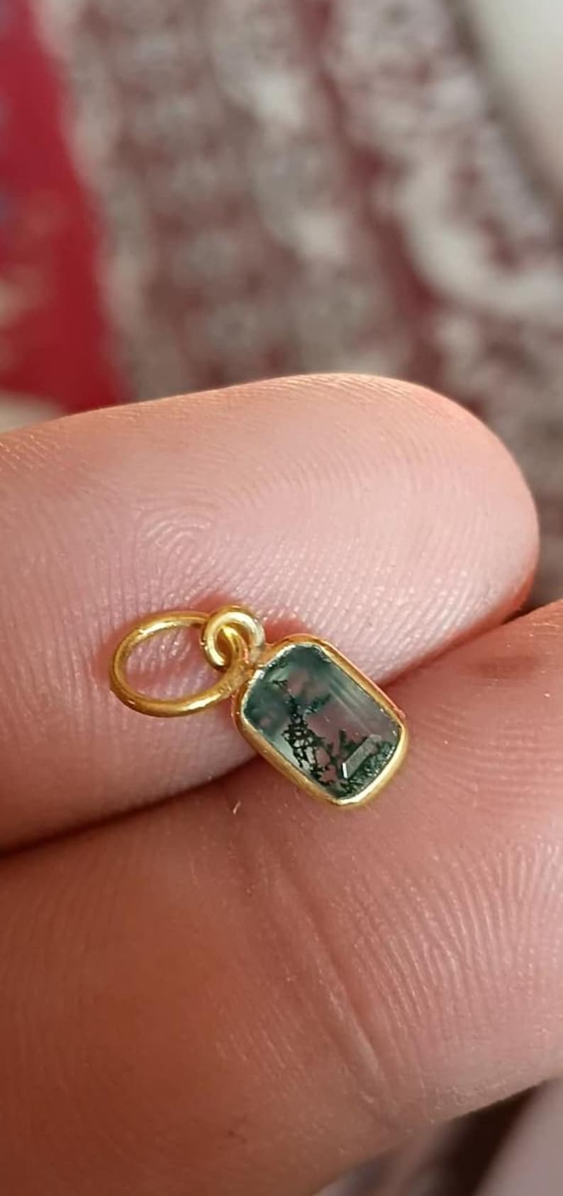 May include: A gold pendant with a rectangular, moss-green gemstone. The gemstone is set in a gold bezel and has a unique, natural pattern. The pendant is attached to a small gold loop.