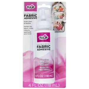 May include: A bottle of Tulip Permanent Fabric Adhesive, 4 fl oz (118 mL), with a white applicator tip. The label features the brand name and product details, including that it dries clear and is washable. The packaging is white and pink.