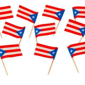 May include: A collection of small Puerto Rican flags on wooden sticks. Each flag features red and white stripes with a blue triangle and a white star. The flags are arranged against a white background.