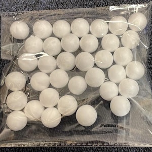 May include: A clear plastic bag filled with numerous white, spherical objects. The spheres appear to be made of a textured material, possibly styrofoam or a similar substance. The bag is sealed, and the contents are densely packed.
