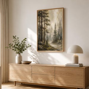 May include: A rectangular framed wall art print depicting a misty forest landscape with tall pine trees, rocky terrain, and a winding path in muted earth tones of green, brown, and beige, displayed in a light wood frame on a plain wall.
