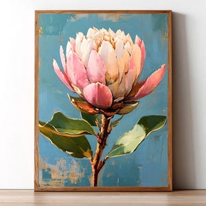 May include: A framed wall art print featuring an oil painting of a single large protea flower with pale pink and white petals. The flower is set against a textured blue background with visible brushstrokes and green leaves on the stem.