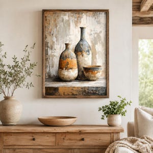 May include: A framed wall art print depicting a still life composition of two ceramic vases and a small bowl. The vessels feature a weathered, textured finish in shades of blue, orange, cream, and brown, set against a neutral, abstract background.