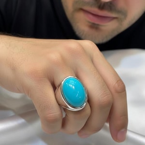 May include: A silver ring with a large, oval, bright turquoise stone. The ring has a polished silver band and a bezel setting that frames the stone. The turquoise stone is a vibrant blue-green color.