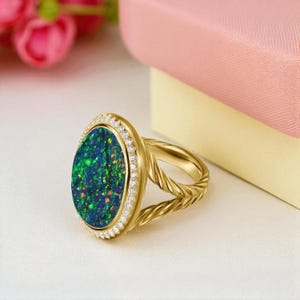 May include: A gold ring featuring an oval-shaped opal with a vibrant display of green and blue hues. The opal is surrounded by a halo of small, clear gemstones. The ring's band has a twisted rope design.