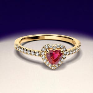 Op de afbeelding: Een gouden ring met een hartvormige rode edelsteen in het midden, omringd door een halo van kleine, heldere edelstenen. De band van de ring is ook versierd met kleine, heldere edelstenen. De achtergrond is een verloop van wit en blauw.