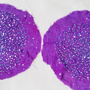 May include: Two circular pieces of purple fabric with frayed edges, each densely embellished with small, reflective circular mirrors and tiny silver sequins scattered across the center, creating a textured and shimmering appearance on the surface.