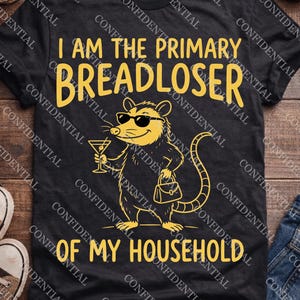 Könnte beinhalten: Ein schwarzes Kurzarm-T-Shirt mit einer gelben Grafik eines Opossums, das eine Sonnenbrille trägt und ein Martiniglas sowie eine Handtasche hält. Der Text I AM THE PRIMARY BREADLOSER OF MY HOUSEHOLD steht in gelben Großbuchstaben darauf.