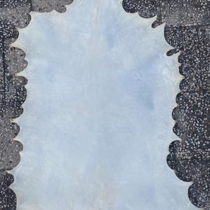 May include: A large, irregularly shaped piece of off-white leather with a scalloped edge. The leather has a smooth surface and a slightly translucent appearance, suggesting it may be thin and pliable. The overall shape is reminiscent of a large leaf or a stylized map.