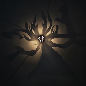 Può includere: Un'applique decorativa con una sorgente luminosa centrale, che proietta un'ombra a forma di albero sulla parete. L'applique ha una finitura scura e la luce crea un'atmosfera calda e accogliente. Il design è artistico e moderno.